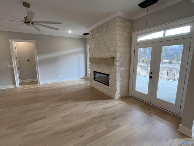 unfurnished living room featuring crown molding, light hardwood / wood-style flooring, a stone fireplace, and french doors