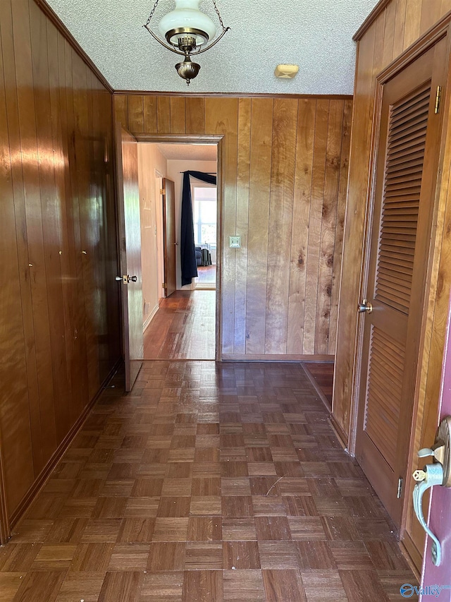 corridor with dark parquet flooring, wood walls, crown molding, and a textured ceiling