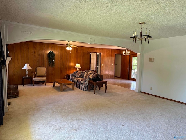 unfurnished living room with ceiling fan with notable chandelier, light colored carpet, wooden walls, and a textured ceiling