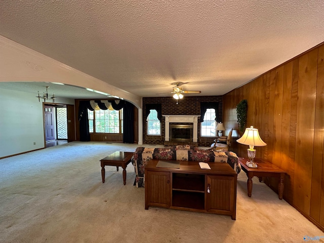 living room featuring a textured ceiling, ceiling fan, light colored carpet, a brick fireplace, and brick wall