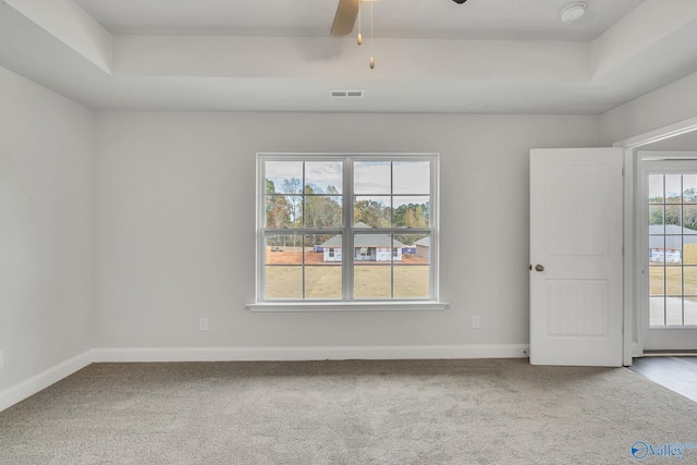 carpeted empty room featuring a tray ceiling, visible vents, ceiling fan, and baseboards