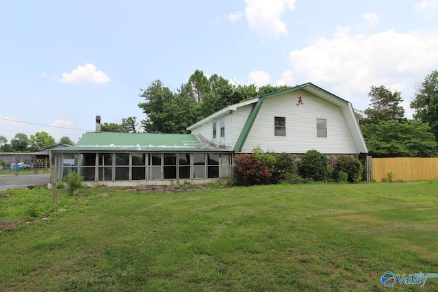 rear view of house featuring a lawn, a gambrel roof, a sunroom, fence, and metal roof