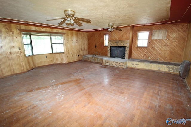 unfurnished living room featuring a stone fireplace, heating unit, a ceiling fan, and wooden walls