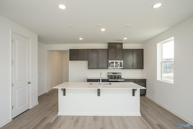 kitchen featuring sink, appliances with stainless steel finishes, a kitchen island with sink, dark brown cabinets, and a kitchen breakfast bar