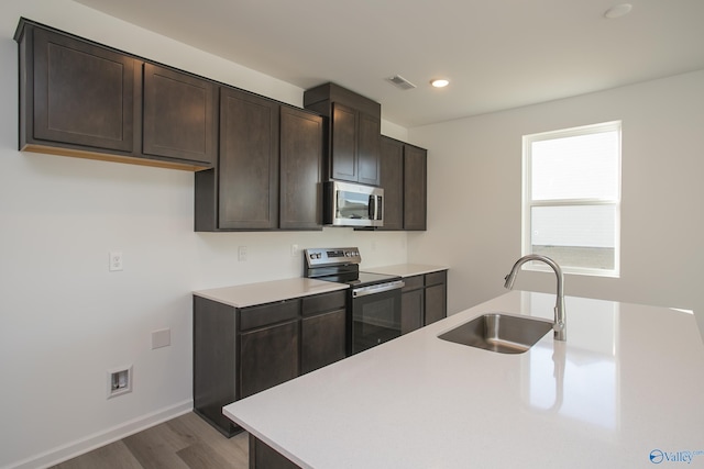 kitchen with appliances with stainless steel finishes, wood-type flooring, sink, and dark brown cabinets