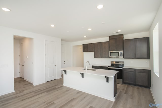 kitchen with sink, stainless steel appliances, dark brown cabinetry, light hardwood / wood-style floors, and an island with sink