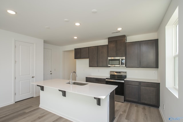 kitchen with sink, dark brown cabinets, light hardwood / wood-style flooring, an island with sink, and stainless steel appliances