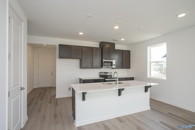 kitchen featuring appliances with stainless steel finishes, a kitchen island with sink, dark brown cabinets, and light hardwood / wood-style floors