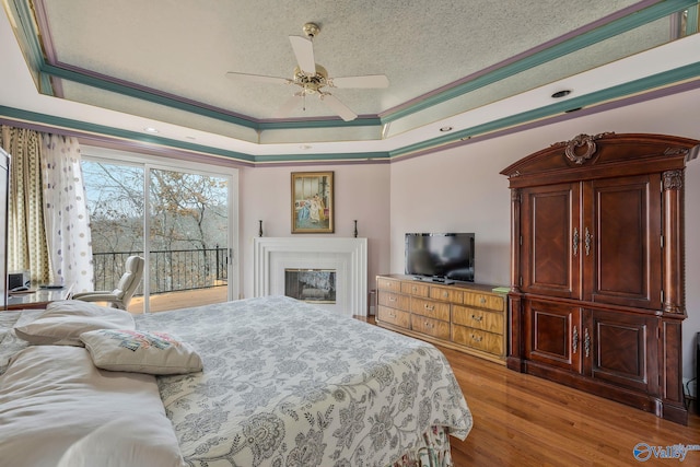 bedroom with ceiling fan, a tray ceiling, crown molding, a textured ceiling, and light hardwood / wood-style flooring