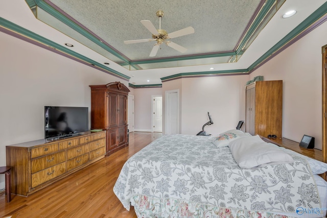 bedroom featuring crown molding, ceiling fan, a tray ceiling, and light wood-type flooring