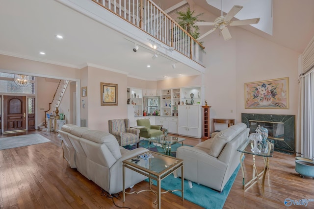 living room featuring a towering ceiling, built in features, a fireplace, ornamental molding, and light hardwood / wood-style flooring