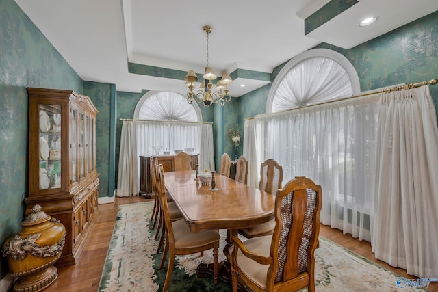 dining area with an inviting chandelier, light hardwood / wood-style floors, and a raised ceiling