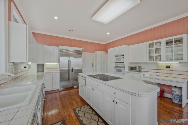 kitchen featuring built in appliances, sink, a kitchen island, and white cabinets