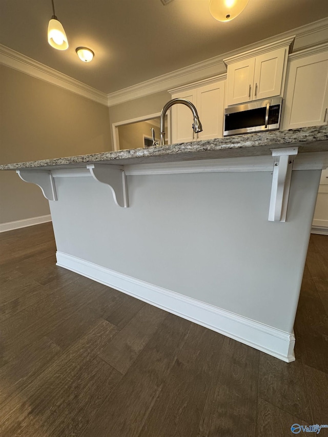 kitchen with a breakfast bar, sink, light stone counters, decorative light fixtures, and ornamental molding