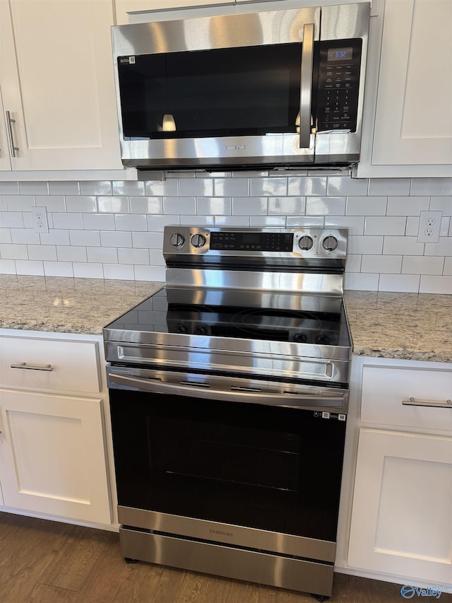 kitchen featuring stainless steel appliances, light stone countertops, white cabinets, and backsplash