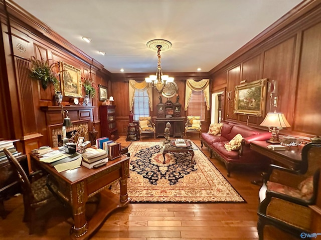 living area featuring wood-type flooring, a chandelier, wood walls, a fireplace, and ornamental molding