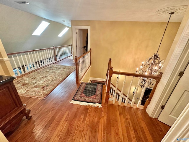 stairs featuring a notable chandelier, vaulted ceiling with skylight, and hardwood / wood-style flooring