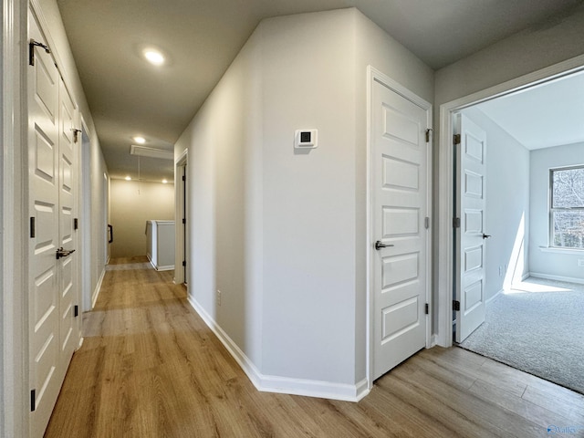 hallway featuring attic access, light wood-type flooring, and baseboards