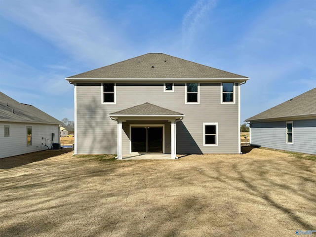 back of property with a patio area, a shingled roof, and central AC