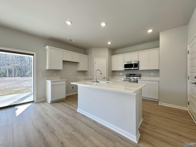 kitchen with a sink, light wood-type flooring, appliances with stainless steel finishes, white cabinetry, and a kitchen island with sink