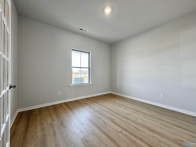 empty room featuring wood finished floors, visible vents, and baseboards