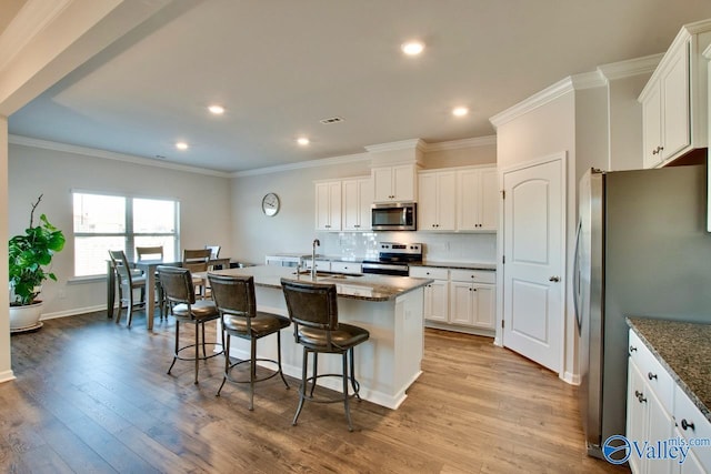 kitchen featuring sink, dark stone countertops, a kitchen island with sink, white cabinets, and appliances with stainless steel finishes