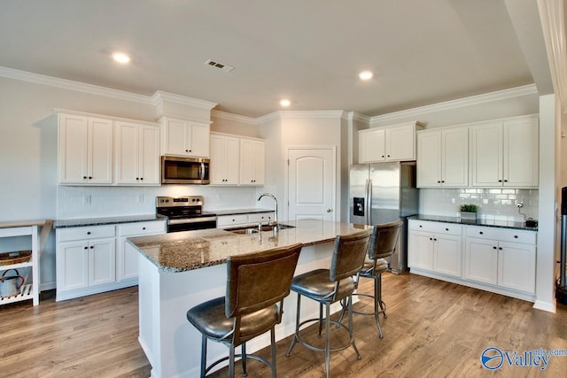 kitchen featuring dark stone counters, white cabinets, sink, an island with sink, and appliances with stainless steel finishes