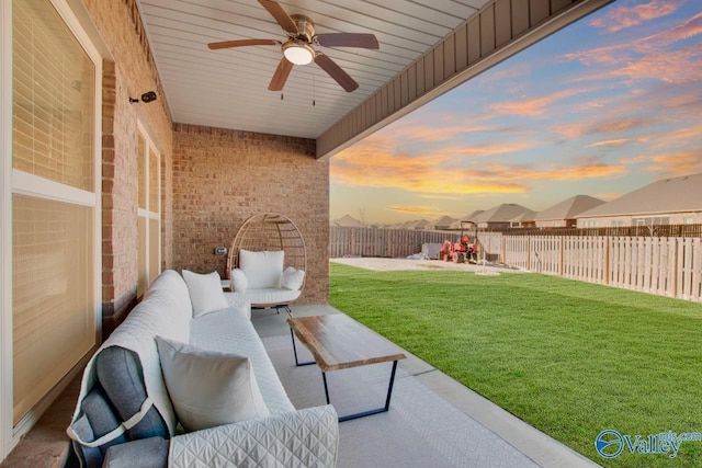 patio terrace at dusk with a lawn, outdoor lounge area, and ceiling fan