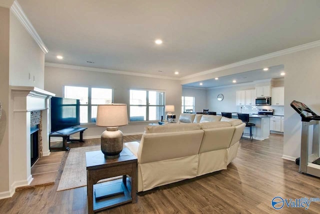 living room featuring light wood-type flooring, ornamental molding, and a tiled fireplace