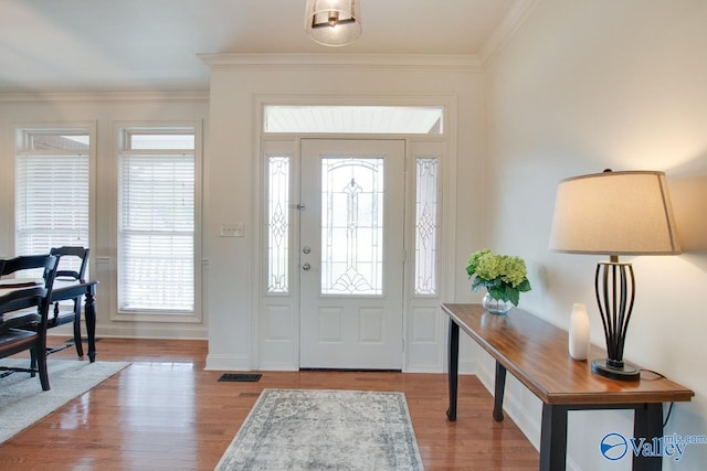 foyer entrance with wood finished floors, a healthy amount of sunlight, crown molding, and baseboards