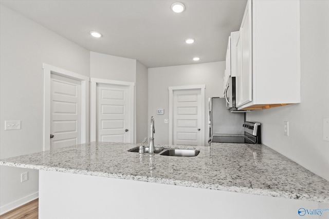 kitchen with light stone countertops, range, white cabinetry, and sink