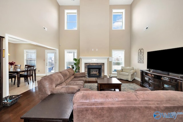 living area featuring a stone fireplace, plenty of natural light, and visible vents