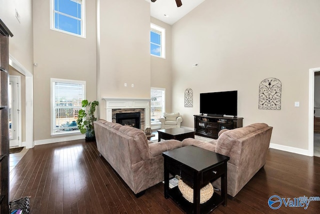 living room featuring ceiling fan, a fireplace, baseboards, and dark wood-style flooring