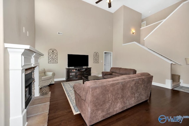 living room featuring ceiling fan, dark wood-type flooring, a fireplace, baseboards, and stairs