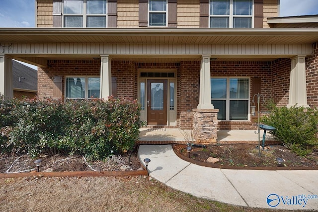 view of exterior entry featuring covered porch and brick siding