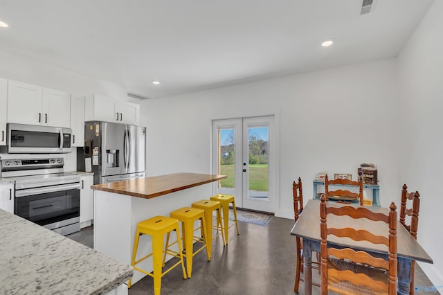 kitchen with a kitchen breakfast bar, french doors, stainless steel appliances, white cabinets, and a kitchen island