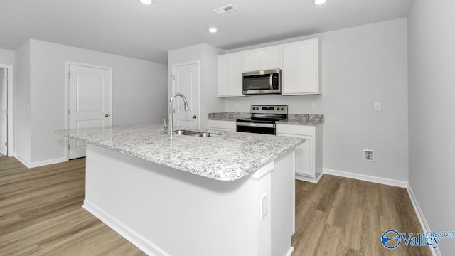 kitchen with stainless steel appliances, sink, white cabinets, light hardwood / wood-style flooring, and a kitchen island with sink