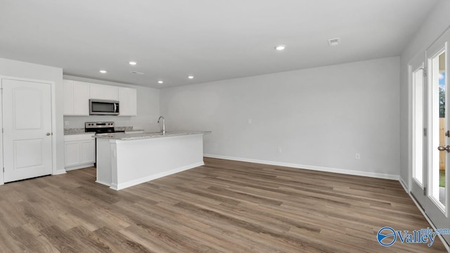 kitchen featuring white cabinets, light hardwood / wood-style flooring, light stone countertops, a center island with sink, and appliances with stainless steel finishes