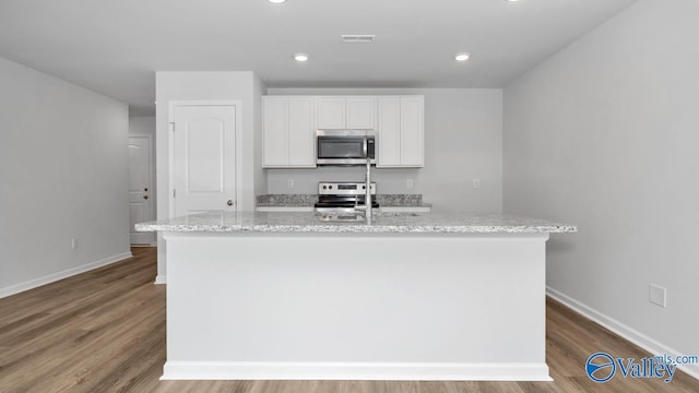 kitchen featuring stainless steel appliances, an island with sink, white cabinetry, and light stone countertops