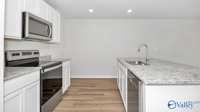 kitchen featuring stainless steel appliances, an island with sink, light stone counters, sink, and white cabinetry