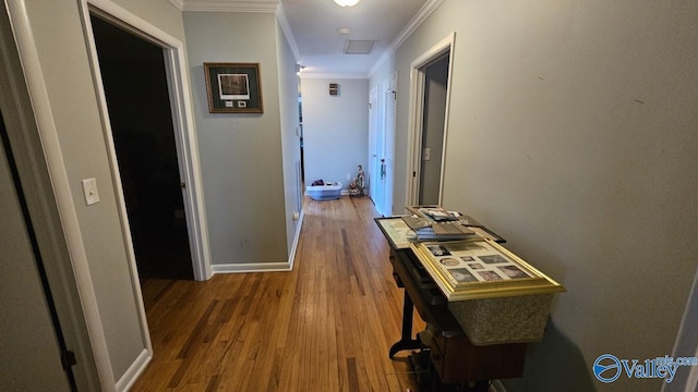 hallway featuring ornamental molding, attic access, baseboards, and wood finished floors