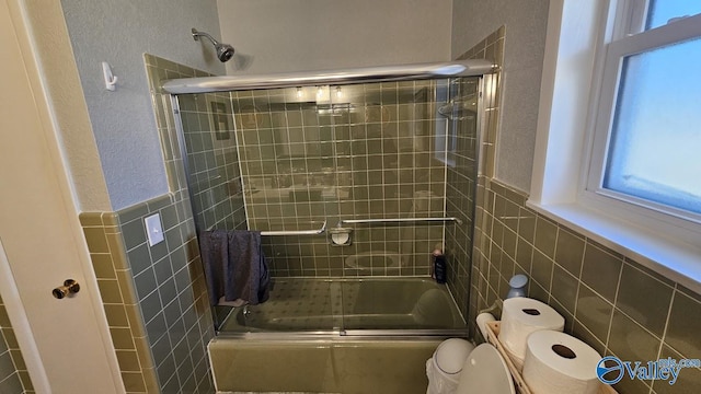 full bathroom featuring a wainscoted wall, tile walls, toilet, and bath / shower combo with glass door