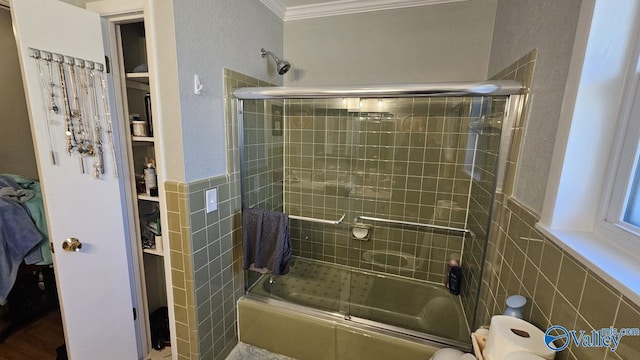 full bathroom with crown molding, bath / shower combo with glass door, tile walls, and wainscoting