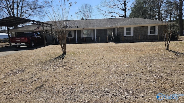 ranch-style house with dirt driveway, brick siding, roof with shingles, and a detached carport