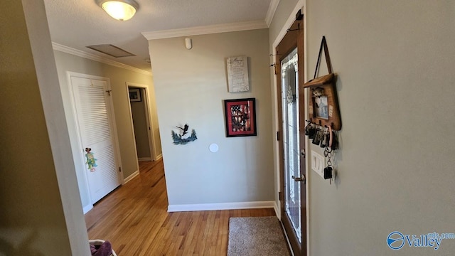 hall with attic access, baseboards, visible vents, ornamental molding, and light wood-style floors