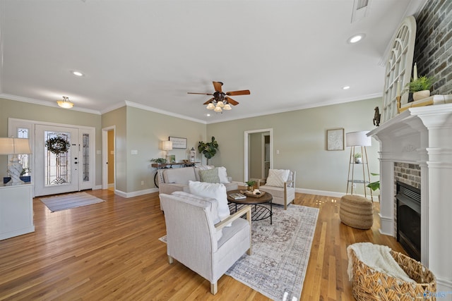 living room with ceiling fan, a fireplace, crown molding, and light hardwood / wood-style flooring