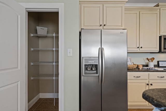 kitchen featuring dark tile patterned floors, cream cabinetry, and appliances with stainless steel finishes