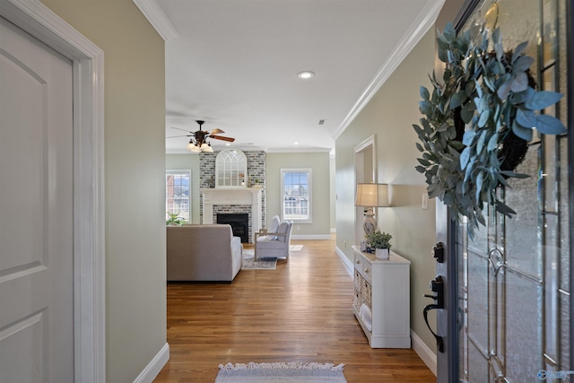 interior space featuring ceiling fan, a fireplace, ornamental molding, and light hardwood / wood-style flooring