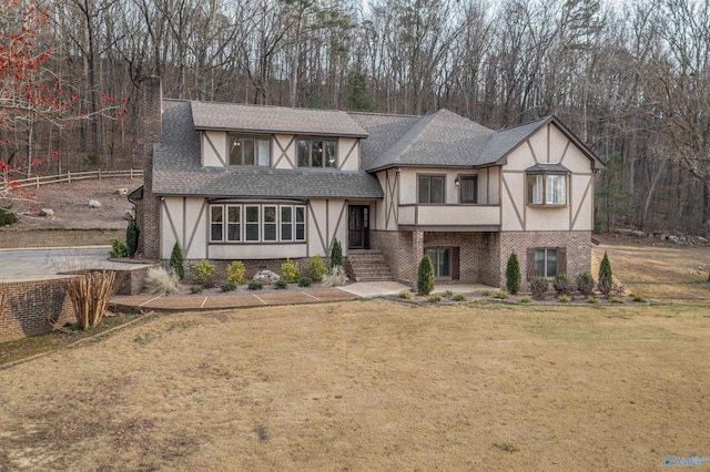 tudor-style house featuring a front lawn, stucco siding, brick siding, and roof with shingles