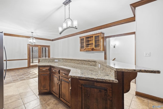 kitchen with a chandelier, crown molding, glass insert cabinets, light stone counters, and pendant lighting
